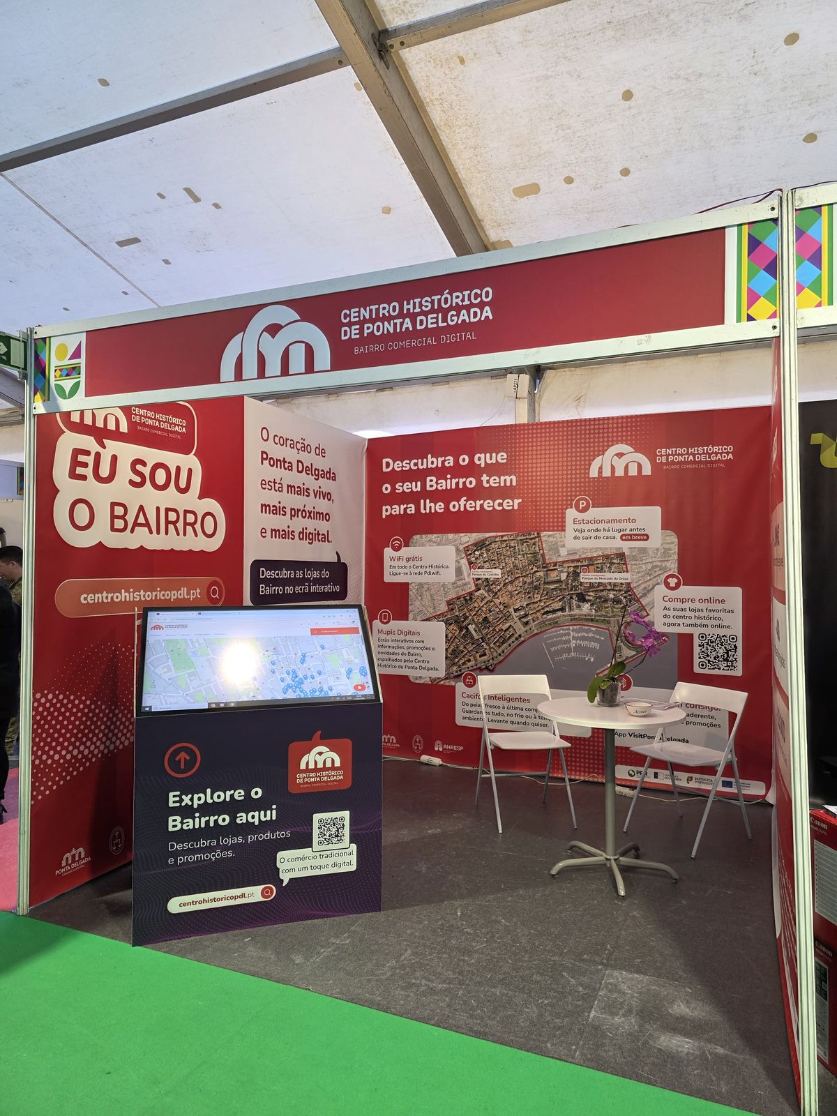Detalhe do stand do Bairro Comercial Digital na FICSA 2026 com balcão de adesão para comerciantes
